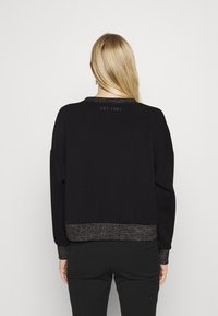 Czarna bluza z luźnym krojem, z metalicznymi akcentami na mankietach i dole, z napisem "EST. 1981" nadrukowanym na tylnym dekolcie. Gładka faktura.