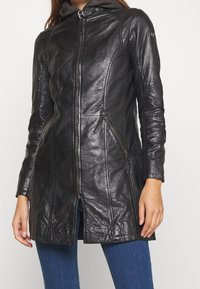 Schwarze Lederjacke mit Reißverschluss vorne, tailliertem Design und seitlichen Reißverschlusstaschen. Sie zeichnet sich durch eine glatte Textur und eine leicht verlängerte Form aus.