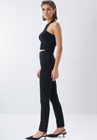 Crni rebrasti crop top s visokim ovratnikom, uparen s crnim hlačama visokog struka i crnim cipelama s oštrim vrhom. Minimalistički dizajn i uski kroj.