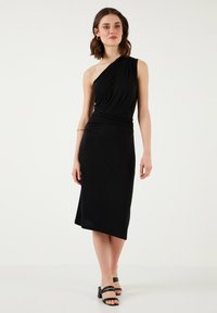 Black, one-shoulder midi dress with a gathered waist and asymmetric hem. Made from soft, stretchy material with a smooth texture. Casual design.