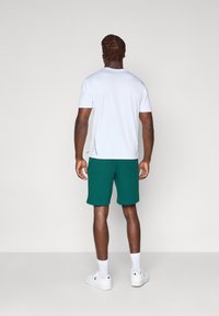 Hvid kortærmet skjorte med rund hals, parret med grønne shorts med snor, og hvide sportssko med logo. Enkel design, afslappet pasform.
