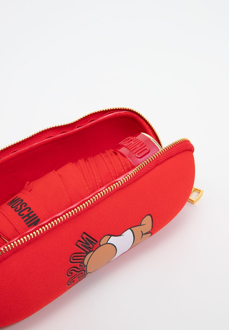 Rotes Moschino-Reißverschlusstäschchen, teilweise offen, mit einem gefalteten roten Regenschirm darin, mit einem Teddybär-Graphic auf der Seite des Täschchens.