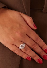 Zilveren ring met een marquise ontwerp, met een grote centrale steen omringd door kleinere edelstenen, gezet op een hand met rode nagellak.