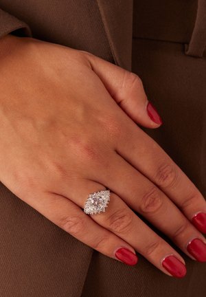 Zilveren ring met een marquise ontwerp, met een grote centrale steen omringd door kleinere edelstenen, gezet op een hand met rode nagellak.