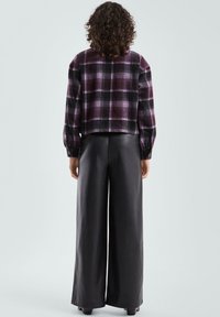 Krótka kratkowana marynarka w kolorach fioletowo-czarnych z długimi rękawami; zestawiona z szerokimi czarnymi skórzanymi spodniami. Widoczna teksturowana powierzchnia i detal z guzikiem.
