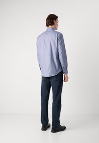 Camicia azzurro chiaro a fantasia con maniche lunghe, polsini con bottone e colletto classico, abbinata a jeans di denim scuro e scarpe nere.