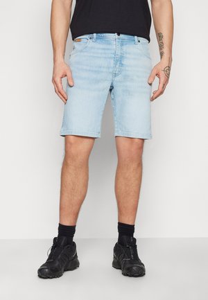 Shorts de denim azul claro con un corte recto, diseño de cinco bolsillos, costuras visibles y una etiqueta de cuero en la cintura. Zapatos y calcetines negros.