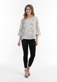 Hvid blomstret skjorte med sorte trykte blomster, flared ærmer, parret med sorte leggings og strappy sorte hæle. Glat stofstruktur.