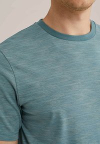 Teal-stribet t-shirt med rund halsudskæring. Fremstillet af et tekstureret stof med subtile linjer og en tætsiddende silhuet.