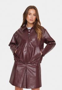 Giacca in pelle borgogna con zip frontale, vestibilità oversized e vita elastica. Presenta due tasche laterali e un colletto a punta.