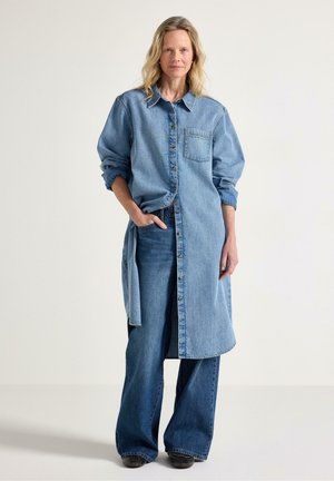 Klänning i ljusblå denim med långa ärmar, en ficka och knappar, kombinerad med vida jeans i mörkare blå denim.