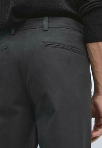 Dark gray trousers with a slim fit, featuring back pockets with subtle stitching and a smooth texture, made from durable fabric.