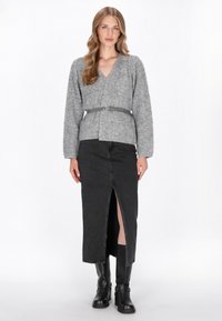 Grijze, fuzzy wikkeltrui met lange mouwen, gecombineerd met een zwarte denimrok met een voorknos. De look wordt compleet gemaakt met zwarte kniehoge laarzen.