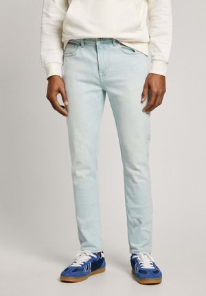 Hellblaue Jeans im Slim-Fit-Stil, mit vorderen Taschen, Reißverschluss und Kontrastnähten. Kombiniert mit blauen Sportschuhen.