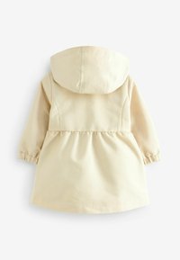 Veste à capuche beige clair avec poignets élastiqués et taille froncée, présentant une texture lisse et un design simple et minimaliste.