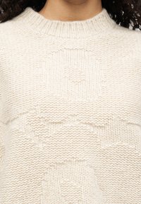 Πλεκτή μπλούζα σε απαλό κρεμ χρώμα με ριμπ λαιμόκοψη. Διαθέτει υφασμάτινα μοτίβα με κύκλους και αστέρια σε όλο το ύφασμα.