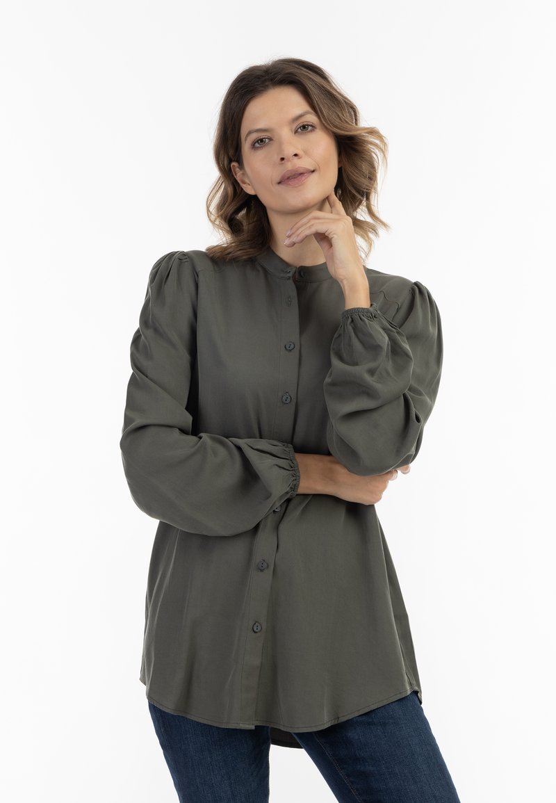 Olijfgroen blouse met knopen en poffende mouwen, zachte stof, afgeronde zoom en subtiele textuur. Beschikt over een Mandarin-kraag en bijpassende knopen.