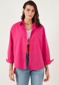Pink button-up shirt made of lightweight fabric, featuring a collar, long sleeves rolled at the cuffs, and a relaxed fit.