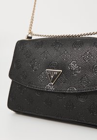 Schwarze Handtasche mit strukturierten Mustern, mit einem dreieckigen Metallsymbol in Gold. Enthält einen goldenen Kettenriemen.