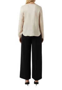 Beżowa bluzka z długim rękawem, okrągłym dekoltem i bufkami, zestawiona z czarnymi spodniami wide-leg o wysokim stanie oraz czarnymi szpilkami.