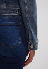 Jeansjacka med ljusblå tvätt, med knappmanschetter och en Lee-märke. Mörkblå jeans med en bakficka synlig.