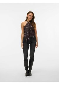 Zwart haltertop met witte stippen en een gestrikte hals, gecombineerd met donkere skinny jeans en zwarte laarzen tot aan de knie. Gladde stof met een aansluitende pasvorm.