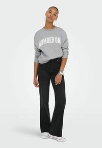 Sudadera gris con el texto "NÚMERO UNO" en blanco, acompañada de jeans negros de tiro alto y campana, y zapatillas blancas. Pendientes de aro circulares.