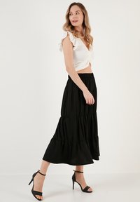 White fitted top with ruffled sleeves, paired with a black tiered maxi skirt. Black heeled sandals complete the outfit. Smooth texture overall.