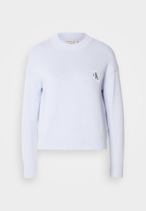 Suéter de punto azul claro con cuello redondo, puños y dobladillo acanalados. Presenta un pequeño parche de logo blanco en el pecho. Textura suave.
