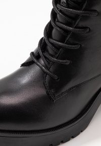 Zwarte leren enkelboot met een glad oppervlak, ronde neus en getextureerde veters. Dikke rubberen zool met profieldetails.