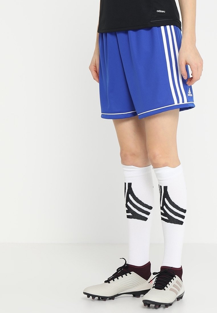 Pantalones cortos de fútbol azules con rayas blancas a los lados y borde blanco. Combinados con calcetas blancas hasta la rodilla con acentos diagonales negros y botas de fútbol grises.
