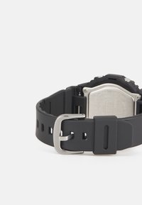 Μαύρο λουράκι ρολογιού από σιλικόνη με ασημένιο μεταλλικό αγκράφα, με ορθογώνιο καντράν και υφή στην πίσω πλευρά. Απλός σχεδιασμός με λεπτομέρειες κοπής.