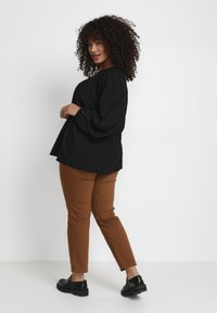 Bluză neagră cu mâneci lungi, cu un croi lejer, asortată cu pantaloni slabi maronii și pantofi negri. Bluză prezintă detalii texturate.