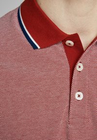 Rode polo shirt met een gestructureerd patroon, voorzien van een gebreide kraag met blauwe en witte strepen en een drie knopenlijst met lichte knopen.
