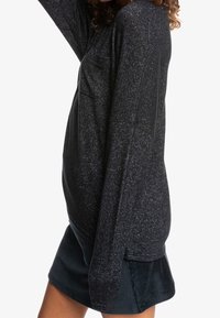Schwarzes Langarmshirt mit einem strukturierten, gesprenkelten Muster und einer Brusttasche, kombiniert mit einem dunkelblauenCordrock.