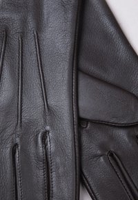 Black leather gloves feature a textured finish, curved seams, and subtle stitching details. The design includes a snug fit with articulated fingers.