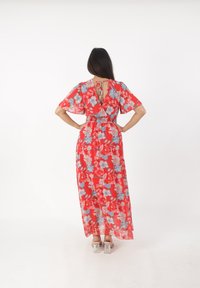 Robe maxi rouge à fleurs avec des manches courtes et flottantes, une taille cintrée et un dos en V profond, ornée de motifs floraux bleu et blanc. Texture transparente.