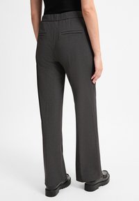 Gray, tailored pants with a flat front, wide legs, and back pockets. Made of textured fabric, resting above black footwear.
