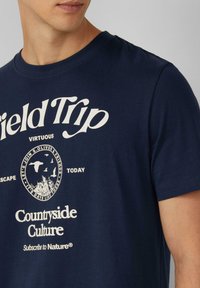 Marineblauwe katoenen t-shirt met witte grafische bedrukking met tekst en een cirkelvormig natuurthema-design. Klassieke ronde halslijn en korte mouwen.