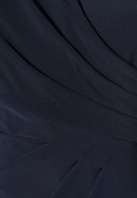 Mörk marinblått tyg med mjuka veck och överlappande lager som skapar ett slätt, strukturerat mönster och subtil textur.