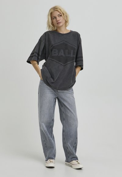 T-shirt gris foncé surdimensionné avec "BALL" imprimé au centre, porté avec un jean taille haute bleu clair et des baskets blanches.