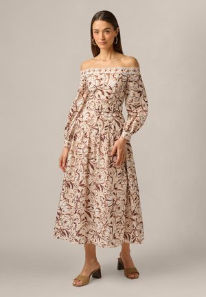Vrouw die een off-shoulder midi-jurk draagt met lange opgepofte mouwen en een bloemmotief, gecombineerd met beige hoge hakken met open teen.