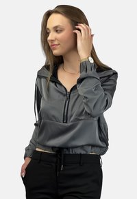 Szara, lekka kurtka zapinana na zamek z kapturem, zebranym dołem, elastycznymi mankietami i bocznymi kieszeniami, zestawiona z czarnymi dopasowanymi spodniami.