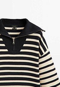 Pull-over rayé avec un motif noir et blanc, doté d'un large col côtelé et d'une fermeture éclair argentée, fabriqué en tissu doux.