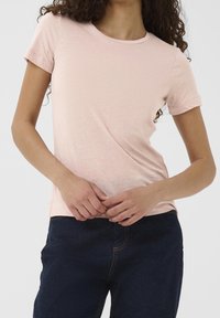 Light pink t-shirt made of soft fabric, featuring a round neckline and short sleeves, worn with dark blue jeans.
