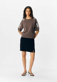 Pull en maille marron avec broderie florale sur les manches, associé à une mini-jupe noire à fente sur le côté et des sandales noires fines.