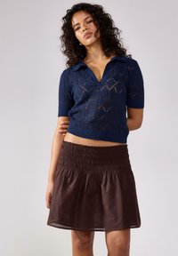 Top in maglia blu navy con maniche corte e motivi a rombi abbinato a una gonna marrone con vita smock. Entrambi i capi sono casual e aderenti.