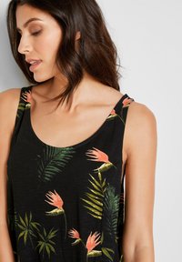 Top senza maniche nero con motivo floreale in cui spiccano foglie verdi e fiori rosa. Tessuto leggero con scollatura rotonda e vestibilità rilassata.