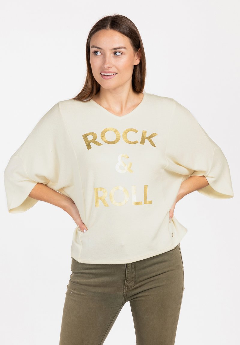 Maglione oversize color crema con scollatura a V e maniche corte. Grafica in foglia d'oro "ROCK & ROLL" sul fronte. Tessuto morbido.