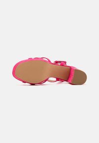 Sandale à talon haut en suède fuchsia avec un bout arrondi, des brides étroites et une semelle en caoutchouc texturé. Le talon est de hauteur moyenne.